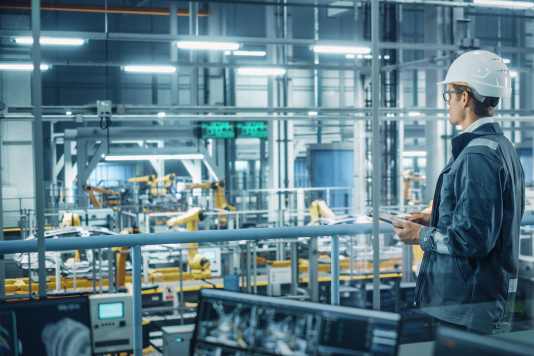 Ingenieur in Uniform und Schutzhelm mit Tablet-Computer in einem Automontagewerk